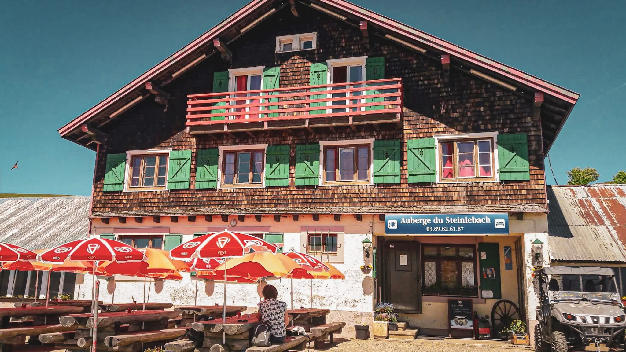 Auberge charmante avec balcon, parasols rouges, idéale pour une pause en randonnée dans les Vosges.