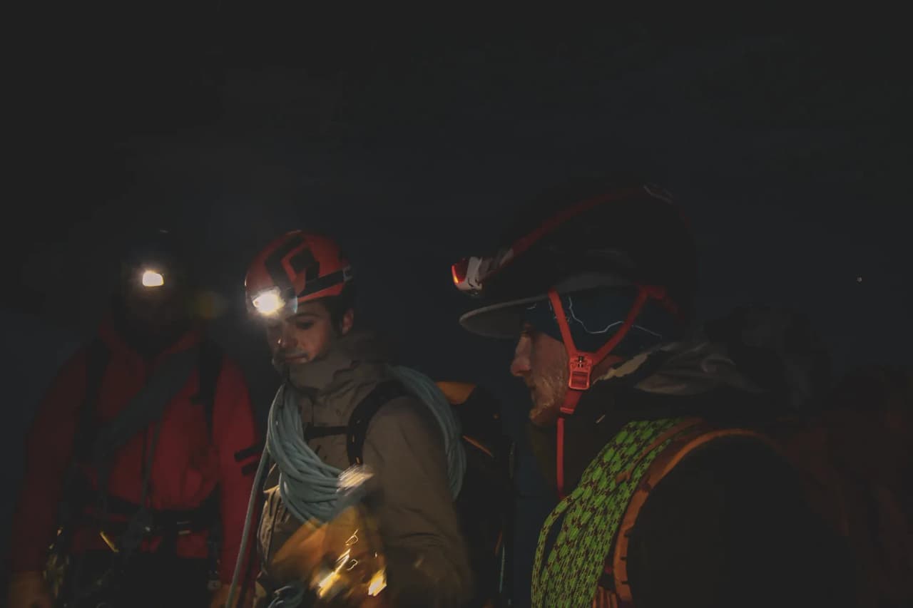 Trois alpinistes équipés de lampes frontales, prêts pour une aventure nocturne en montagne.