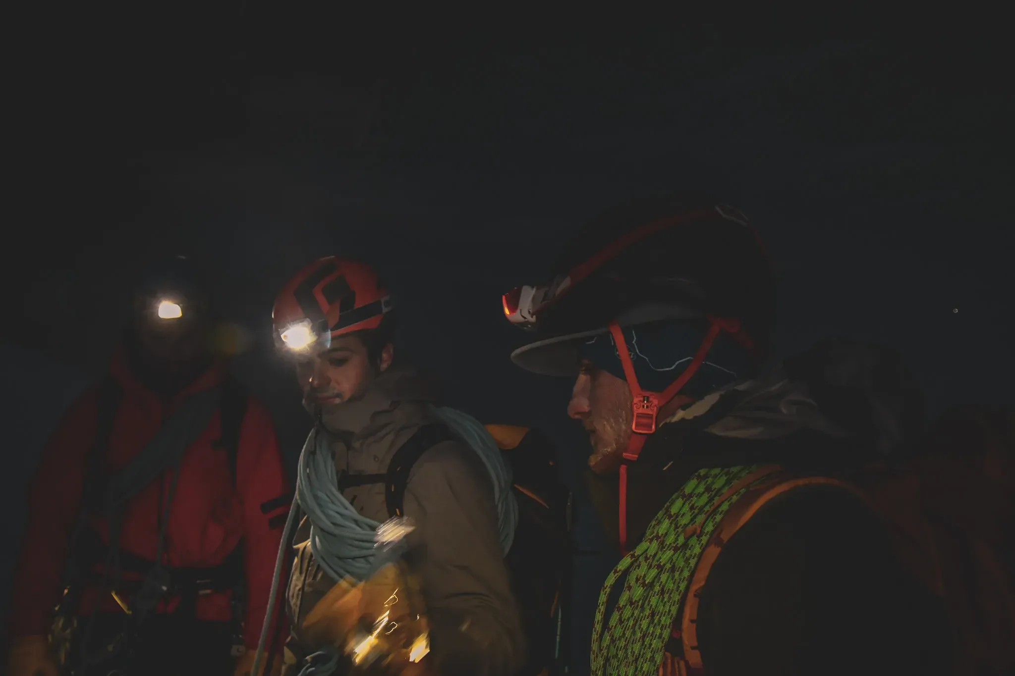 Trois alpinistes équipés de lampes frontales, prêts pour une aventure nocturne en montagne.