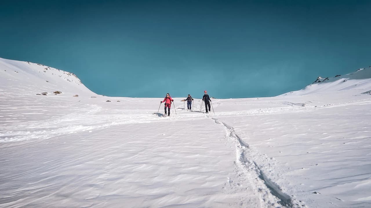 Three walkers are making their way through a pristine winter landscape beneath a brilliant blue sky.