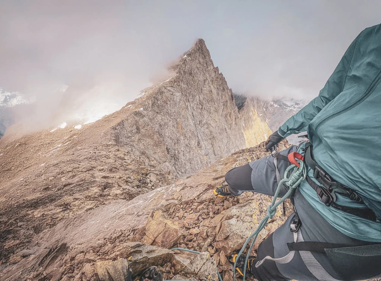 A climber on a rocky ridge with a spectacular view of the Écrins.