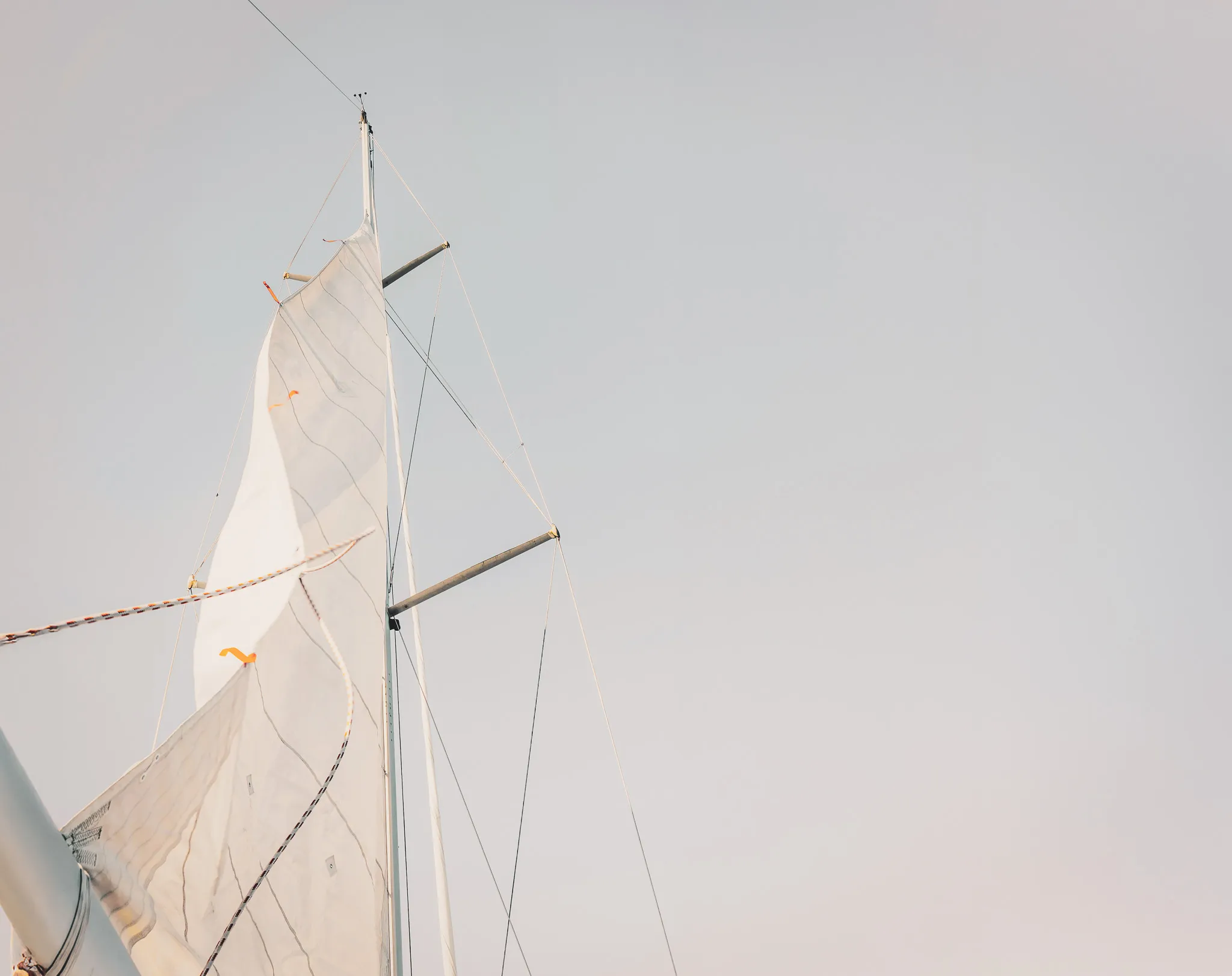 Voile blanche d'un bateau s'élevant vers un ciel lumineux, invitant à l'aventure maritime.