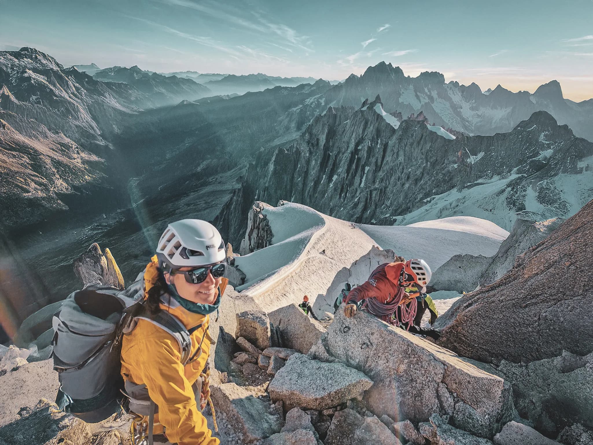 Un groupe de randonneurs escalade des rochers, avec des montagnes majestueuses en arrière-plan.