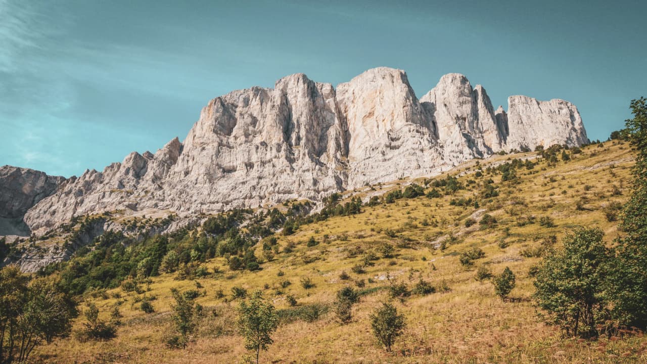 Majestueuses falaises blanches surplombant des prairies verdoyantes, nature envoûtante du Vercors.