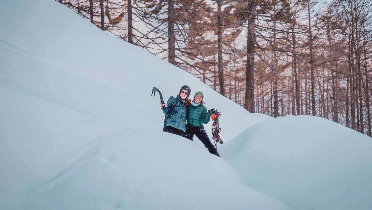 Two smiling people on an ice expedition, surrounded by snow and fir trees in the Alps.