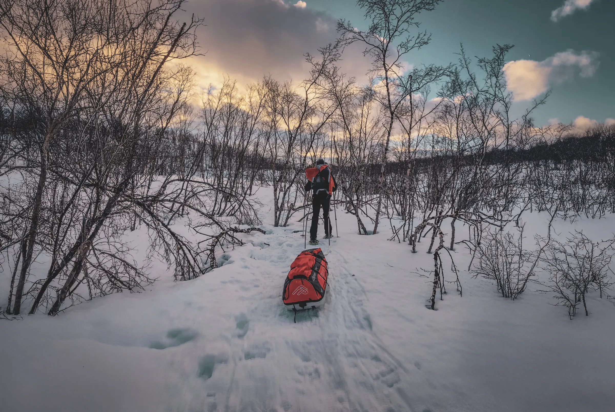 Randonneur en raquettes sur la Kungsleden, tirant une pulka, paysage enneigé et ciel coloré.