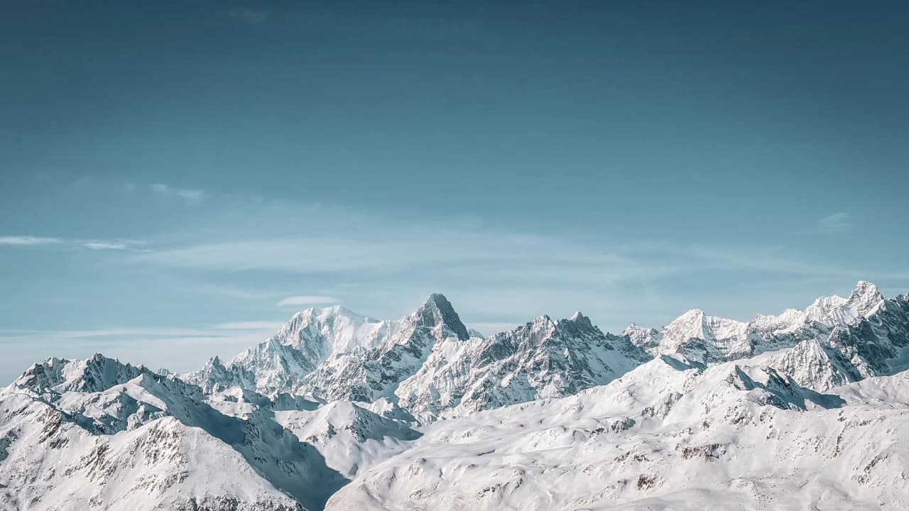 Majestic snow-capped peaks under a blue sky, an invitation to alpine adventure.