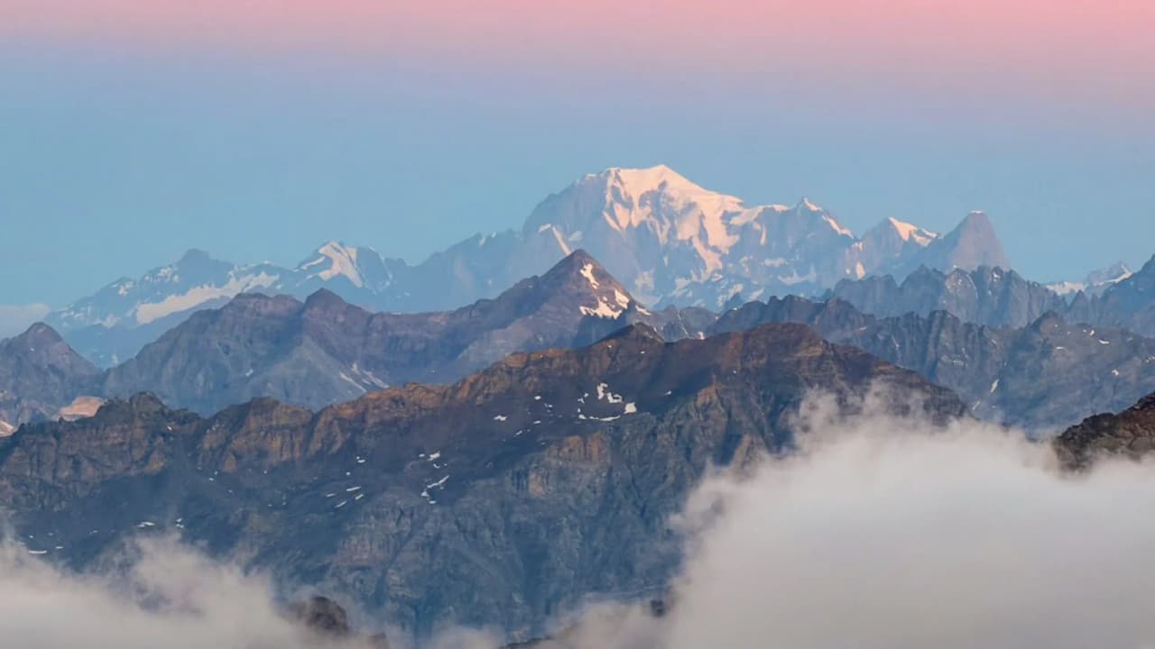 A majestic snow-capped peak, surrounded by impressive mountains beneath a pastel-coloured sky.