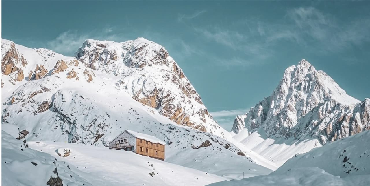 A wooden Mountain hut set in a snow-covered alpine landscape, surrounded by majestic mountains.