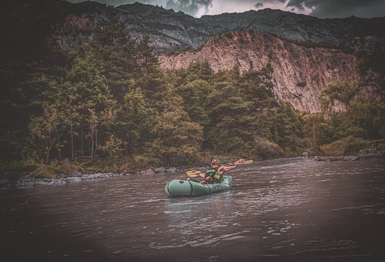 A packraft adventurer navigates a river surrounded by majestic cliffs.