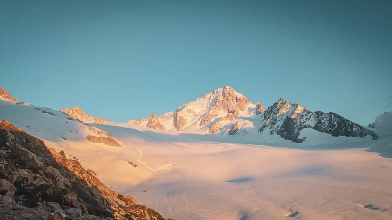 The majestic peak of Mont Blanc against a blue sky, bathed in the first rays of the sun.