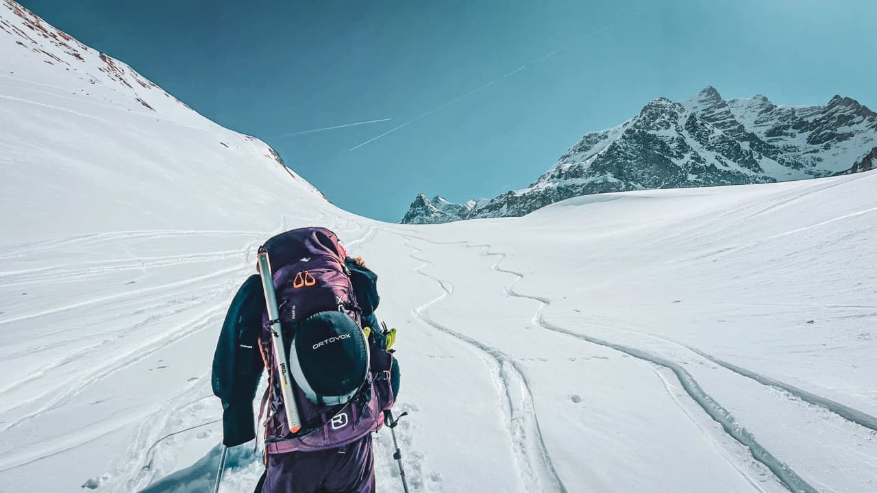 A hiker climbing snow-covered slopes under a blue sky, surrounded by majestic Alpine peaks.