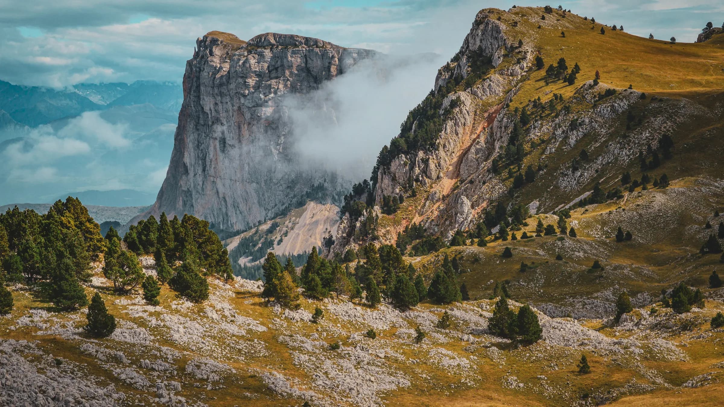 Montagnes majestueuses du Vercors, balisées de nuages, entourées de forêts verdoyantes.