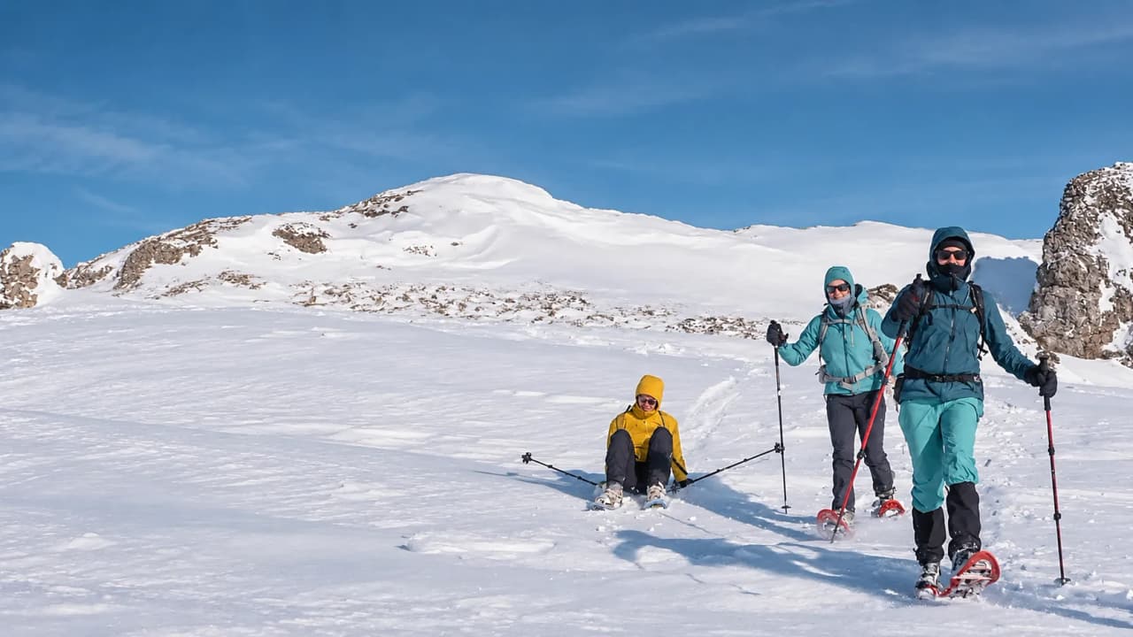 Three snowshoe walkers are enjoying the snow-covered landscape of the Vercors under a brilliant blue sky.