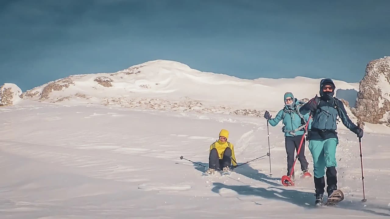Trois randonneuses en raquettes dans la neige, paysages majestueux des montagnes en arrière-plan.