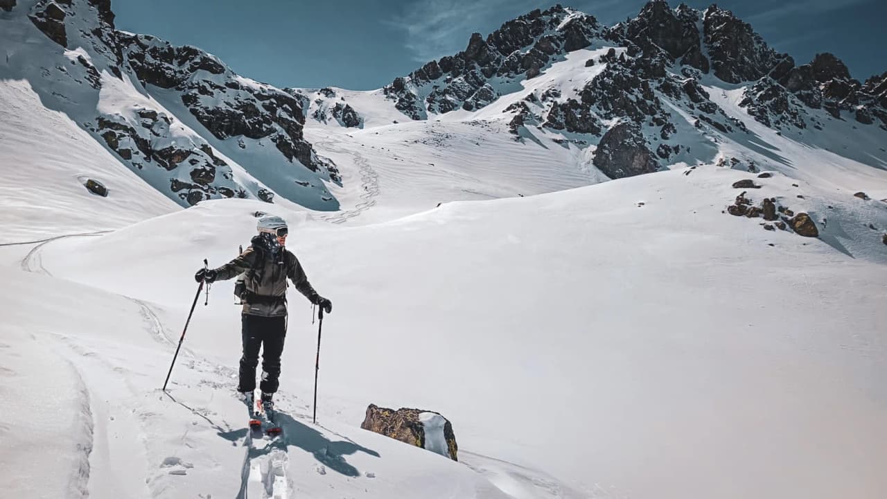 Une skieuse solitaire traverse un paysage enneigé, avec des montagnes majestueuses en arrière-plan.