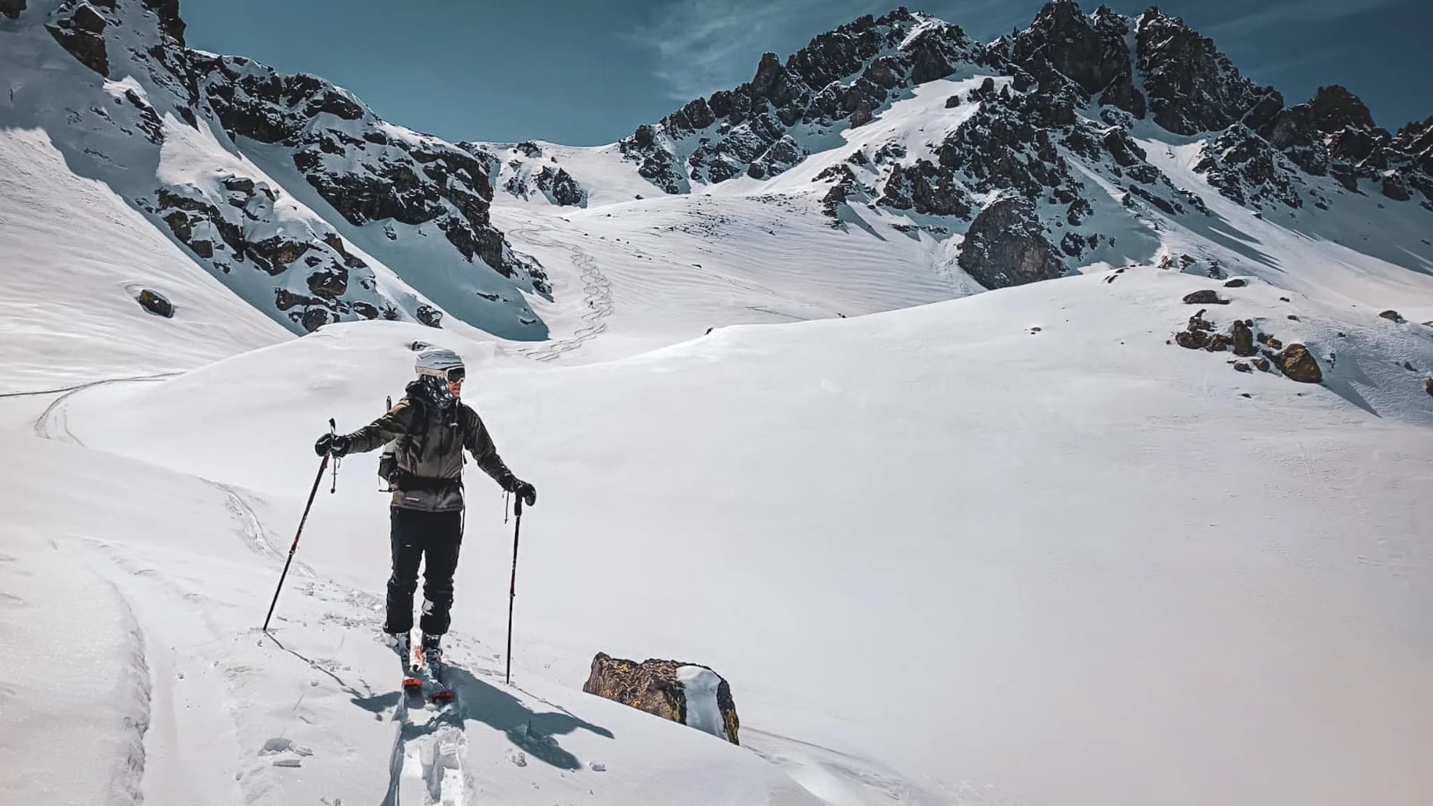 Une skieuse solitaire traverse un paysage enneigé, avec des montagnes majestueuses en arrière-plan.