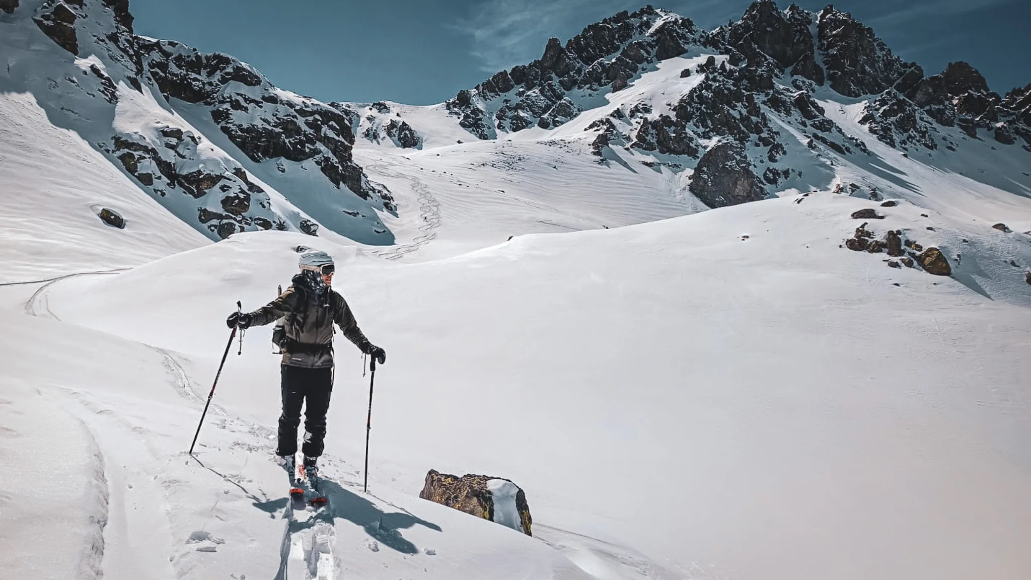 Une skieuse solitaire traverse un paysage enneigé, avec des montagnes majestueuses en arrière-plan.