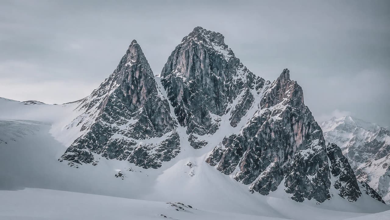 Three majestic snow-capped mountains under dramatic skies, a captivating natural spectacle.