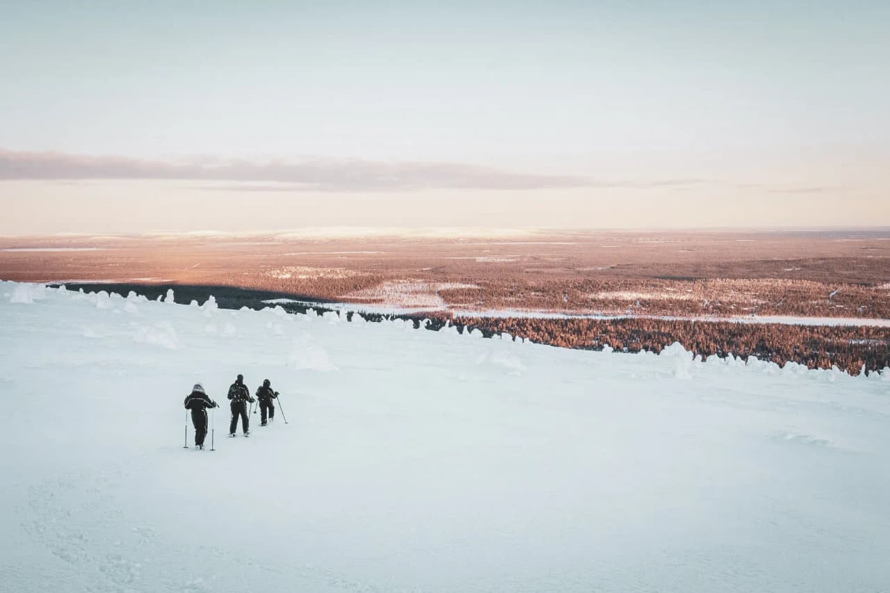 Trois randonneurs traversent un paysage enneigé à couper le souffle en Laponie finlandaise.