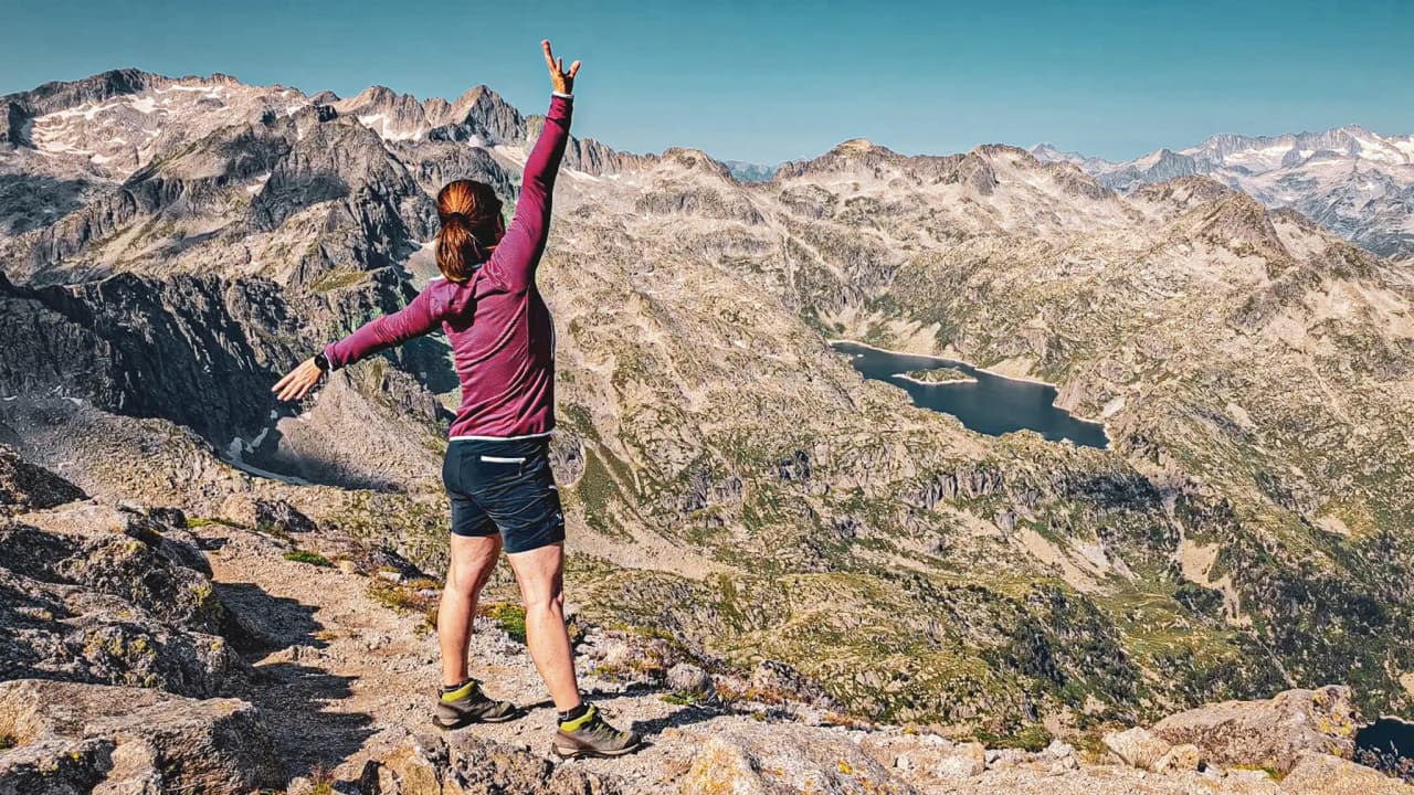 Panoramic view from a Pyrenees summit, with an exhilarated hiker and lakes below.