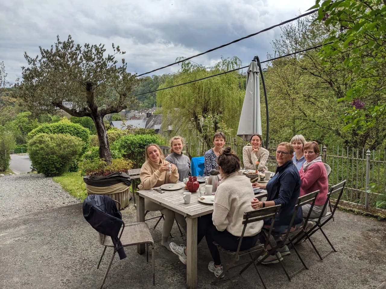 A smiling group around an outdoor table, enjoying a convivial moment in the middle of green countryside.
