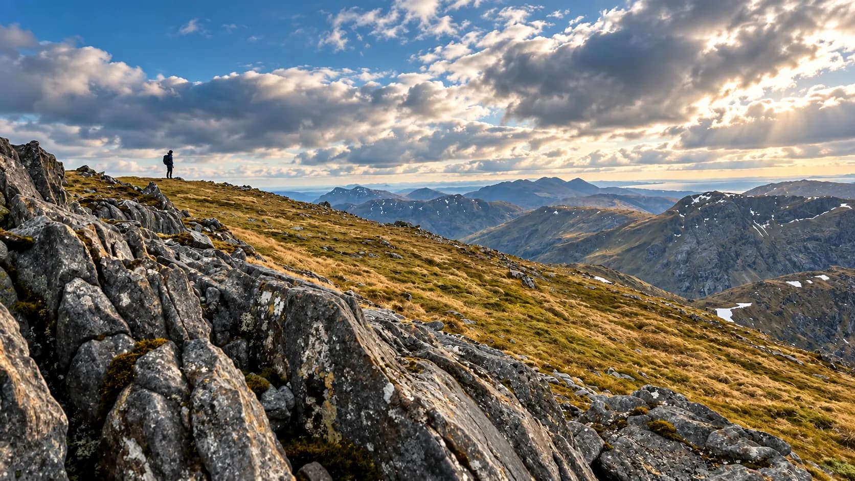 Een wandelaar op een rotsige bergkam aan het eind van de dag, met uitzicht op de bergen van de Highlands