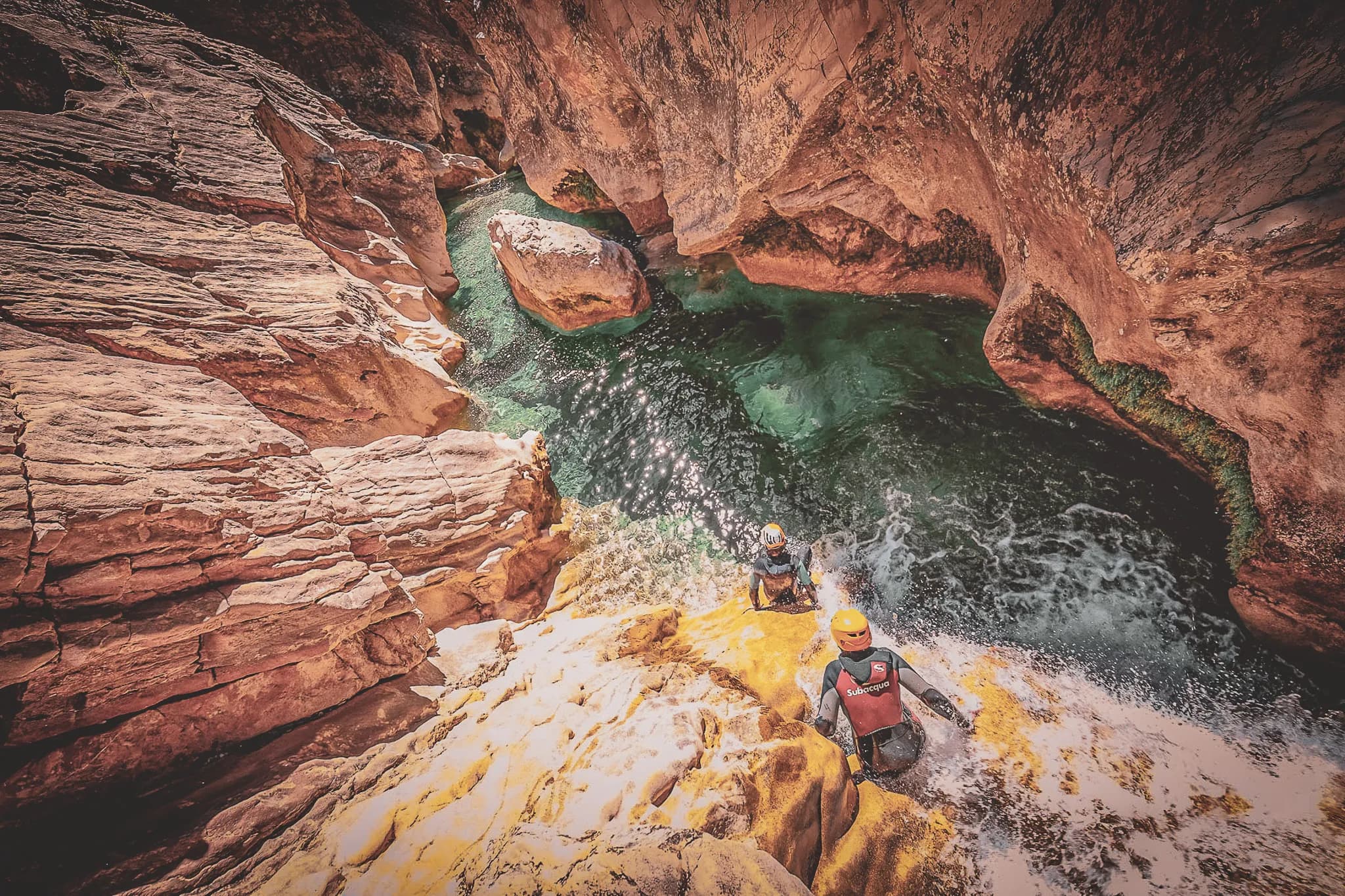 Three canyoning adventurers descend steep cliffs to sparkling turquoise waters.