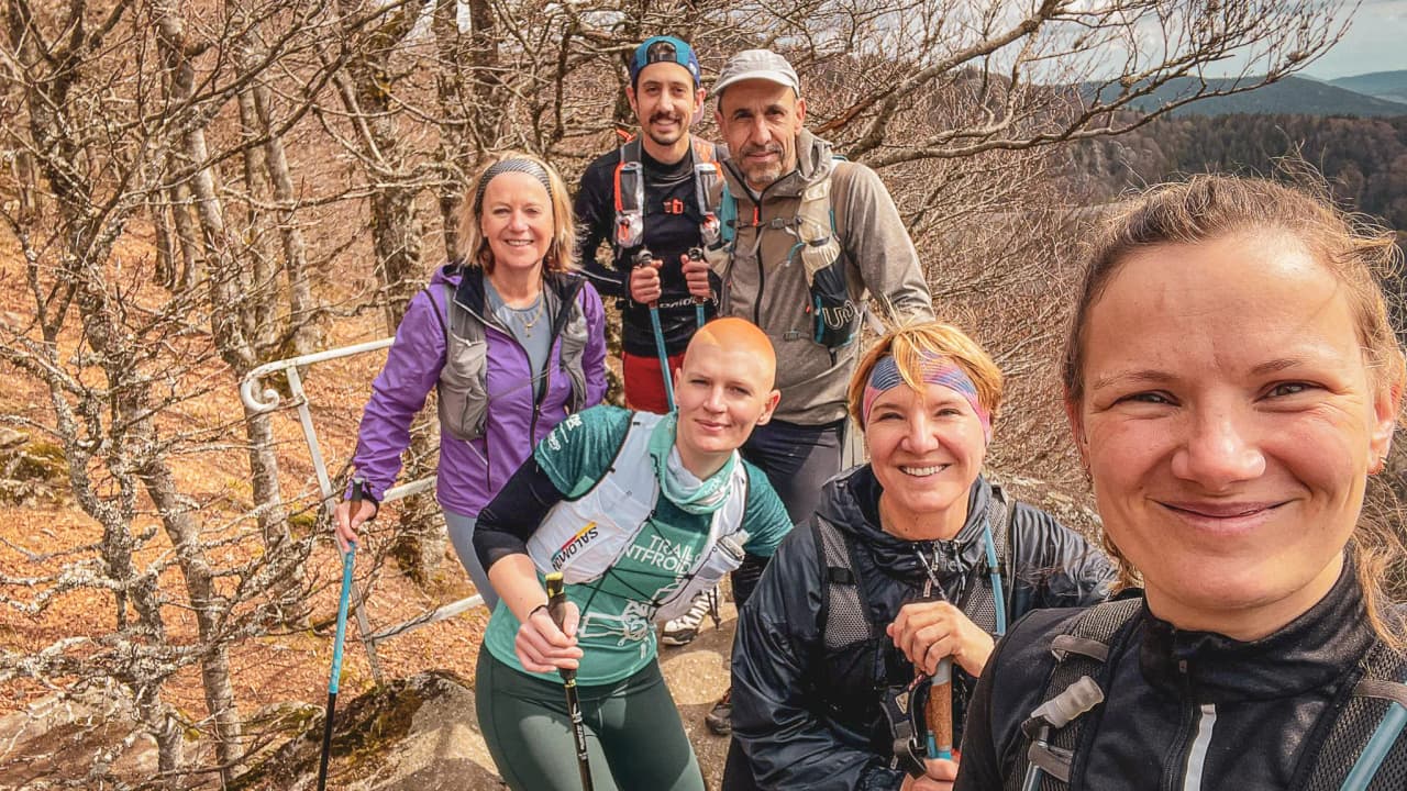 Un groupe souriant de randonneurs en montagne sous un ciel clair, prêts pour l'aventure dans les Vosges.