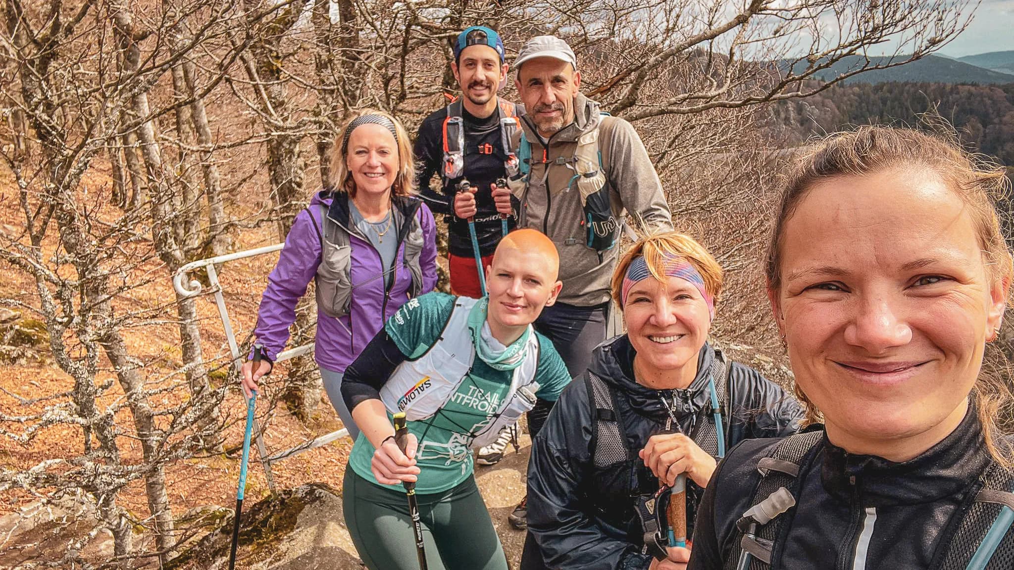 Un groupe souriant de randonneurs en montagne sous un ciel clair, prêts pour l'aventure dans les Vosges.