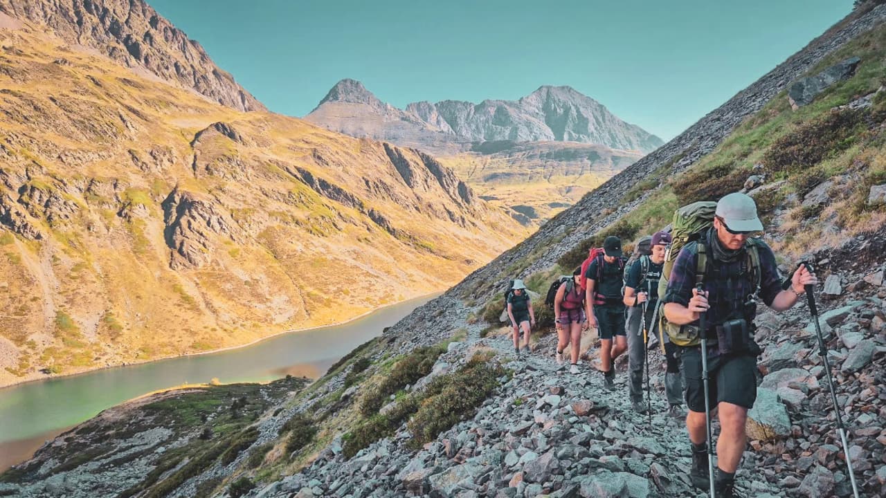 Een groep wandelaars die een steil pad in de Hautes-Pyrénées beklimt, omringd door bergen.