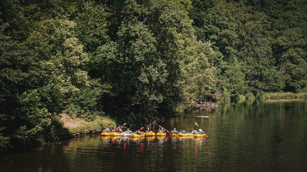 Een groep in packrafts die op een rivier vaart, omringd door groen en vredige landschappen.