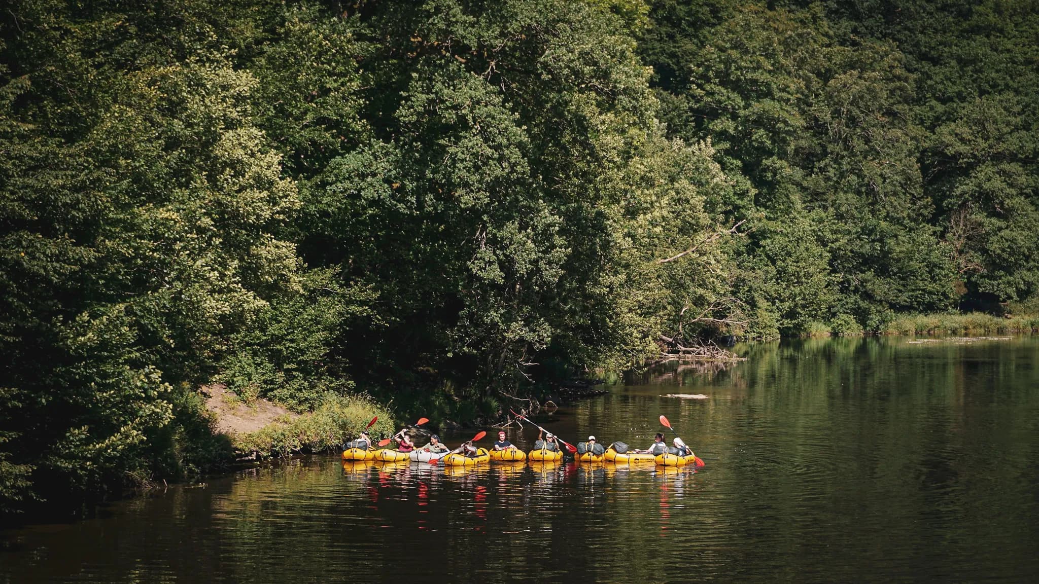 Groupe en packraft naviguant sur une rivière, entouré de verdure et de paysages paisibles.