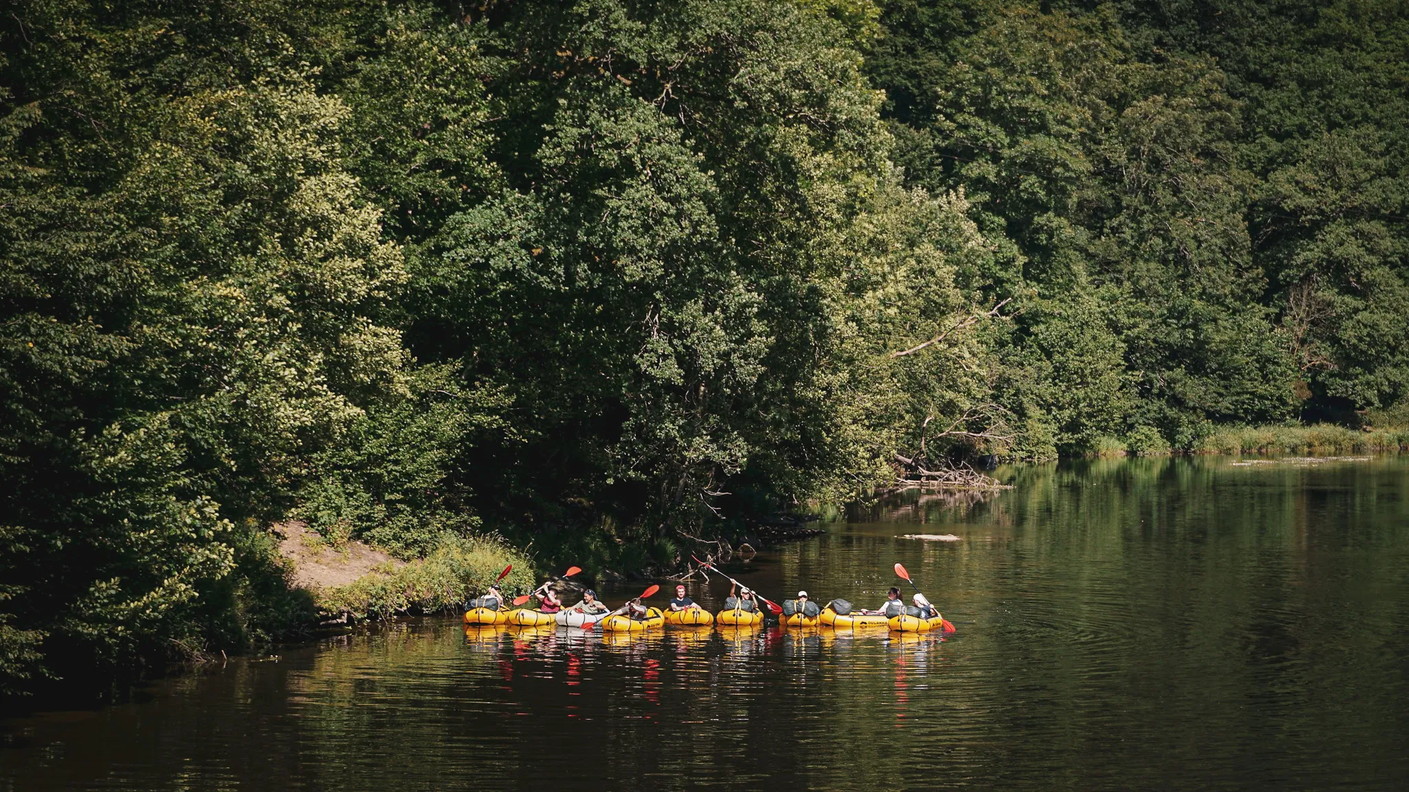 Groupe en packraft naviguant sur une rivière, entouré de verdure et de paysages paisibles.