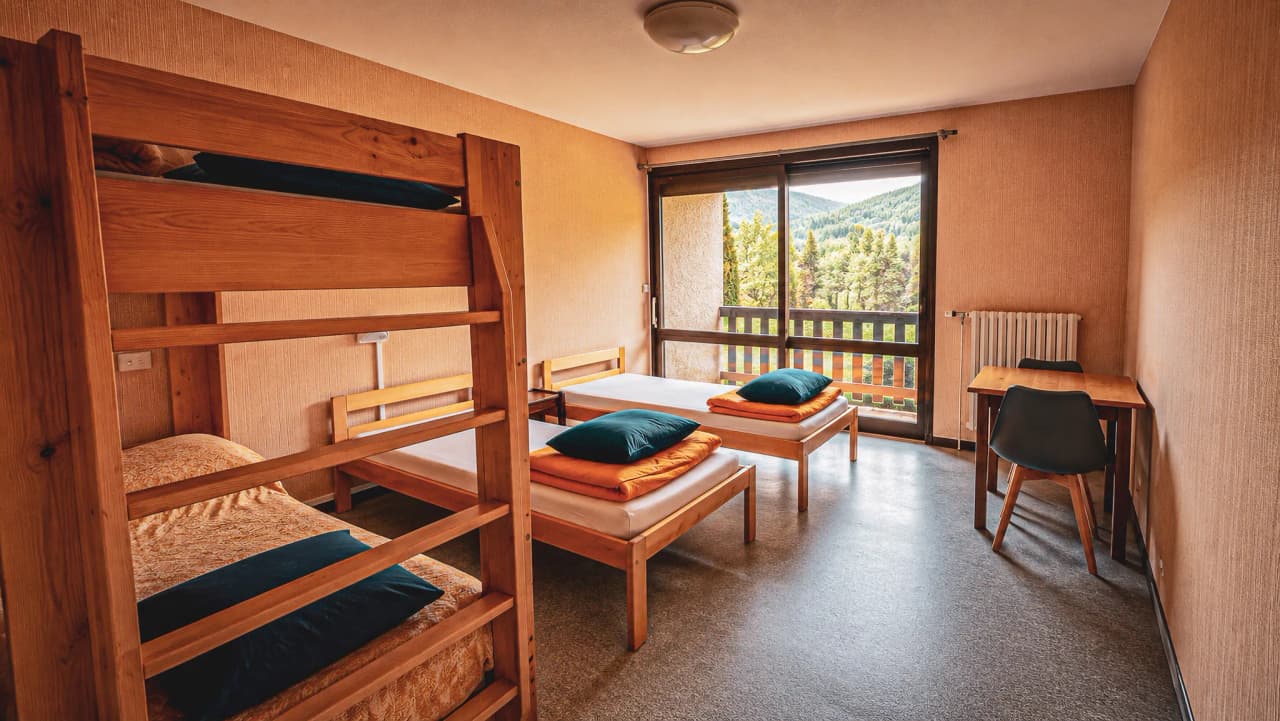 Chambre lumineuse avec lits en bois, vue sur nature, parfaite pour une expédition en montagne.
