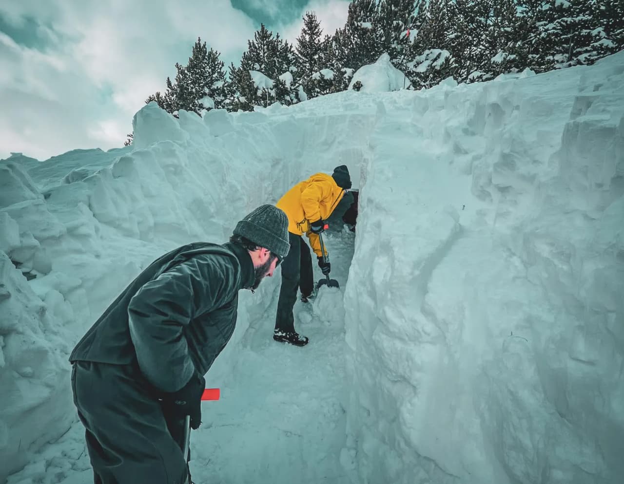 Twee mensen graven een iglo in prachtige sneeuw, omringd door Alpenlandschap.