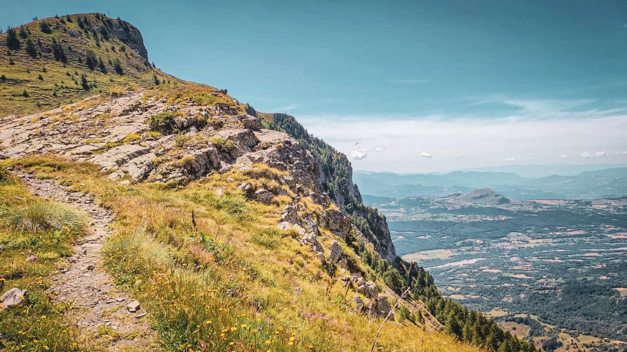 A winding path on the mountainside, overlooking lush green valleys under an azure sky.