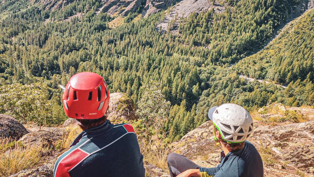 Deux personnes en casque admirent une vue spectaculaire sur une vallée boisée depuis une falaise.