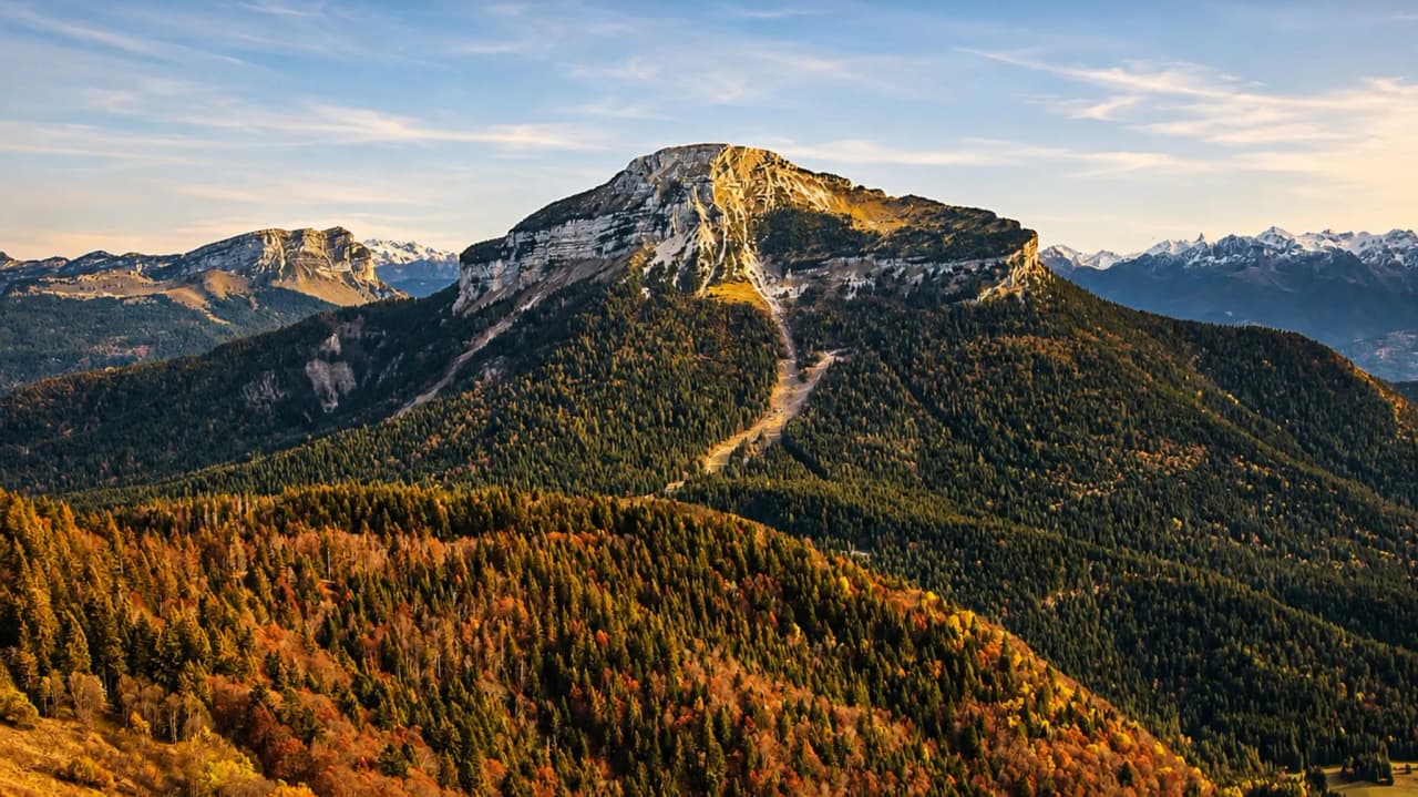 Montagne majestueuse illuminée par le soleil, entourée de forêts d’automne, invitation au trek.