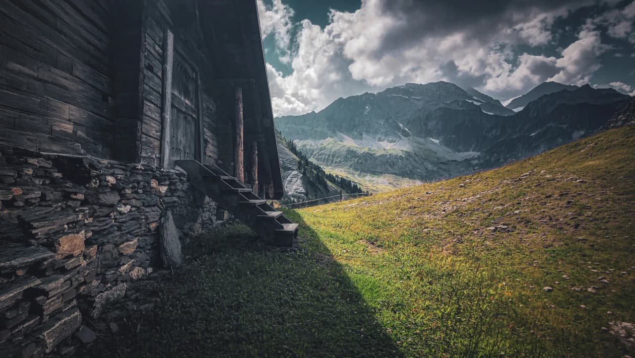 A charming wooden hut at the foot of the majestic Alps, under a cloudy sky.