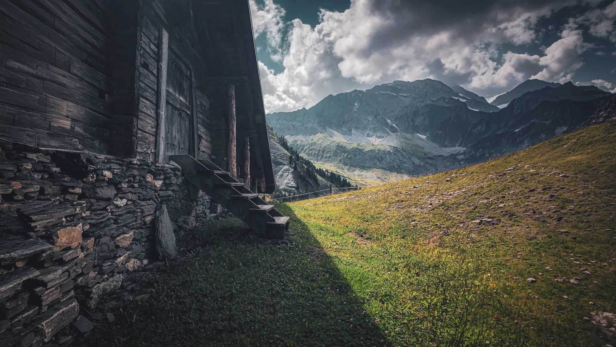 Une charmante cabane en bois au pied des majestueuses montagnes alpines, sous un ciel nuageux.