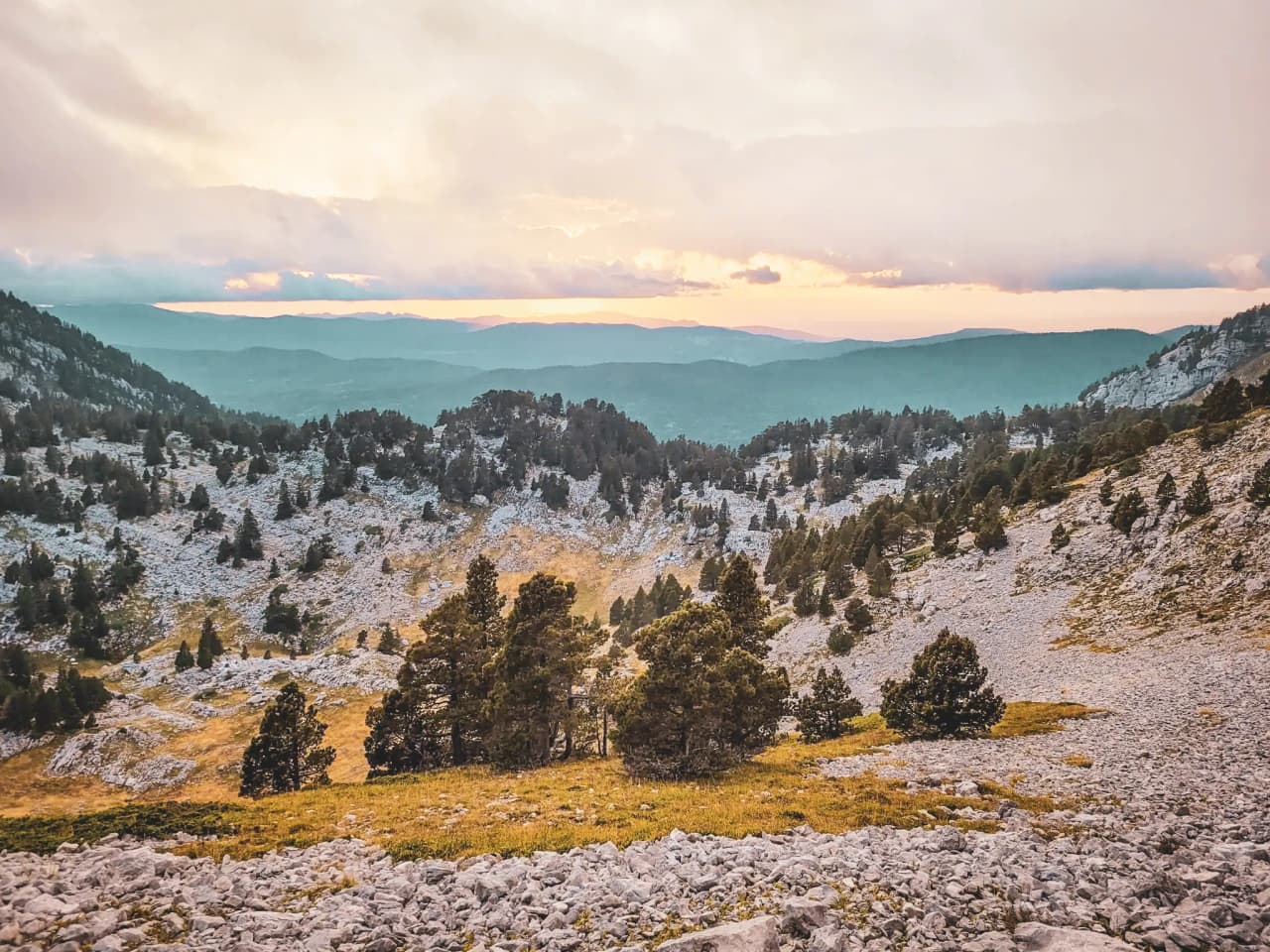 Een berglandschap in de Vercors, met bomen en heuvels onder een kleurrijke hemel bij zonsondergang.