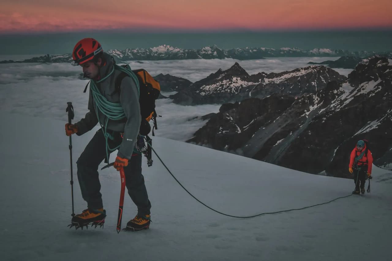 Alpinistes gravissant un glacier au Mont Rose, avec un lever de soleil éclatant en toile de fond.