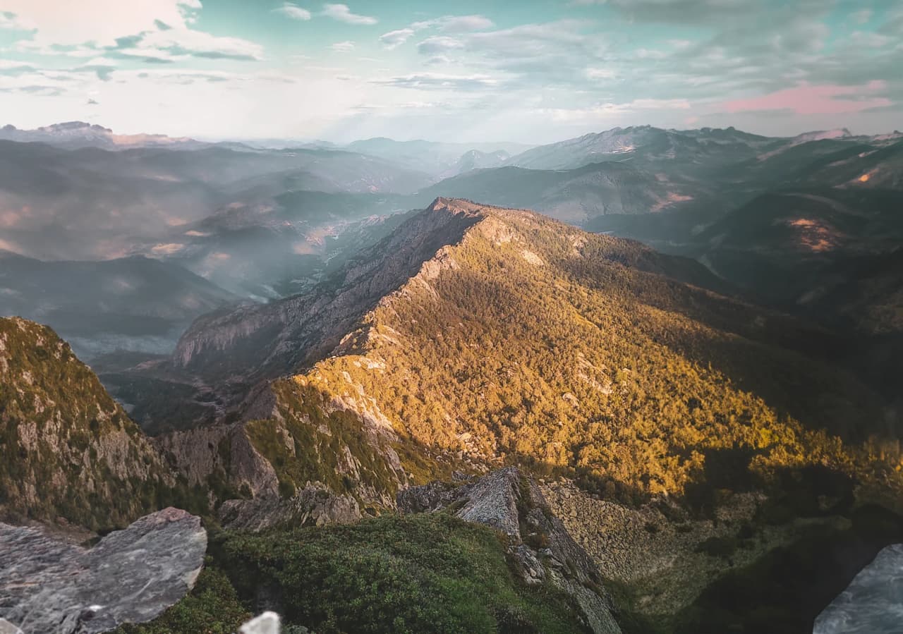 Vue panoramique des Pyrénées, montagnes majestueuses et paysages verdoyants au crépuscule.