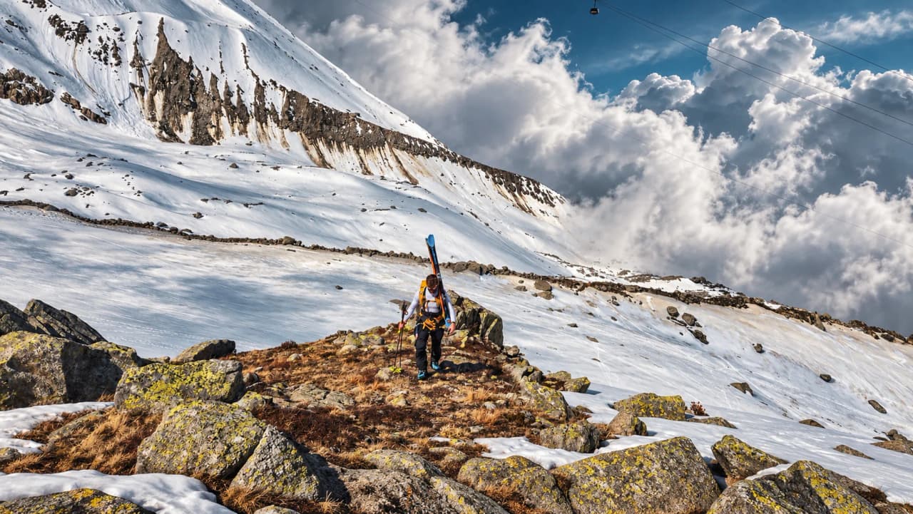 Alpiniste en ski de randonnée sur les pentes enneigées du Mont Blanc, paysage majestueux et nuageux.