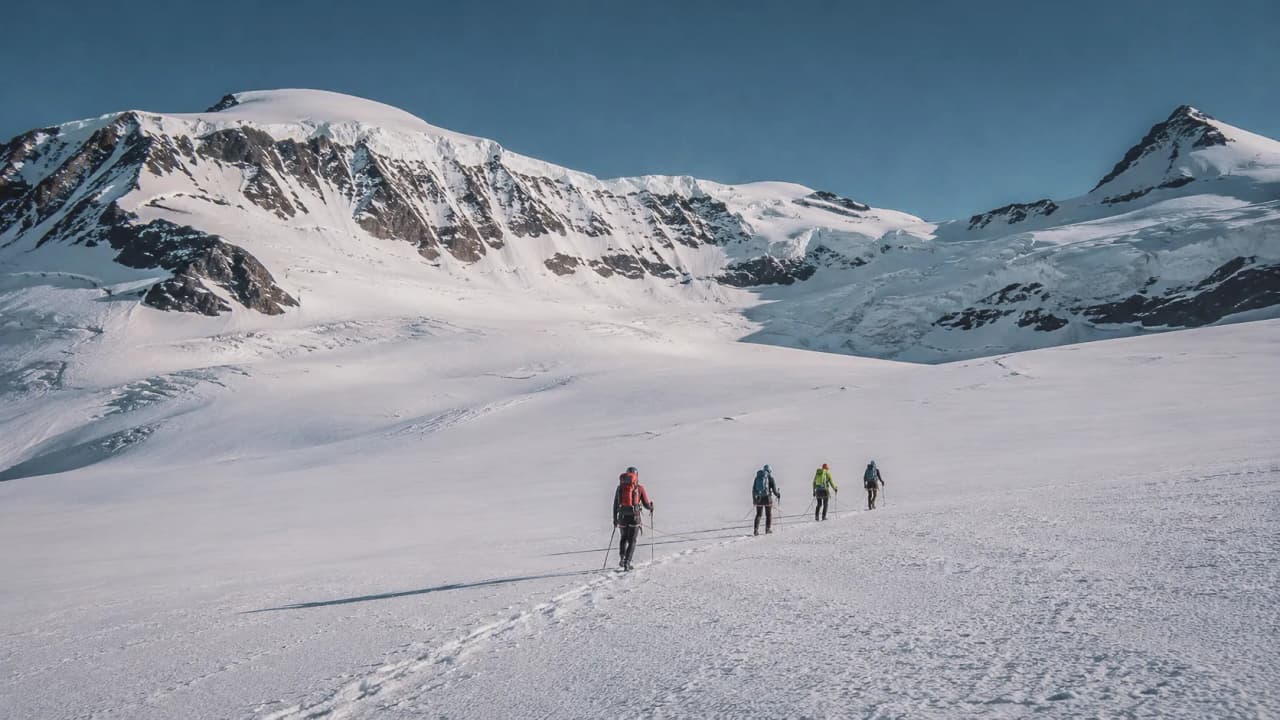 A group of mountaineers making their way across a vast glacier, with majestic snow-capped mountains in the background.