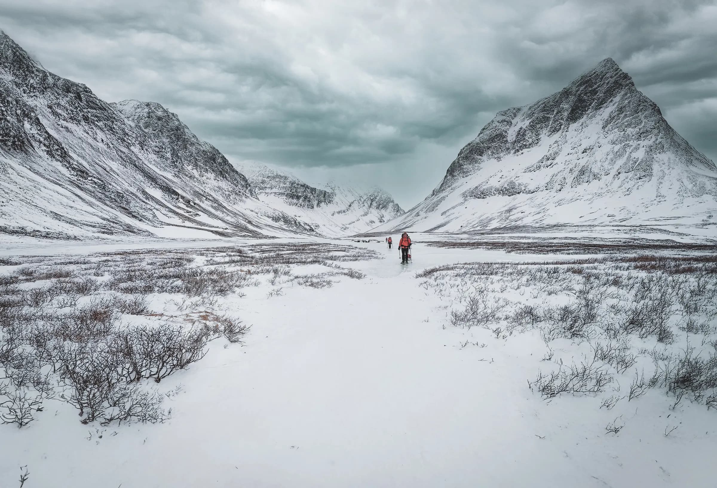 Des randonneurs en raquettes s'avancent dans un paysage enneigé, entourés de montagnes majestueuses.