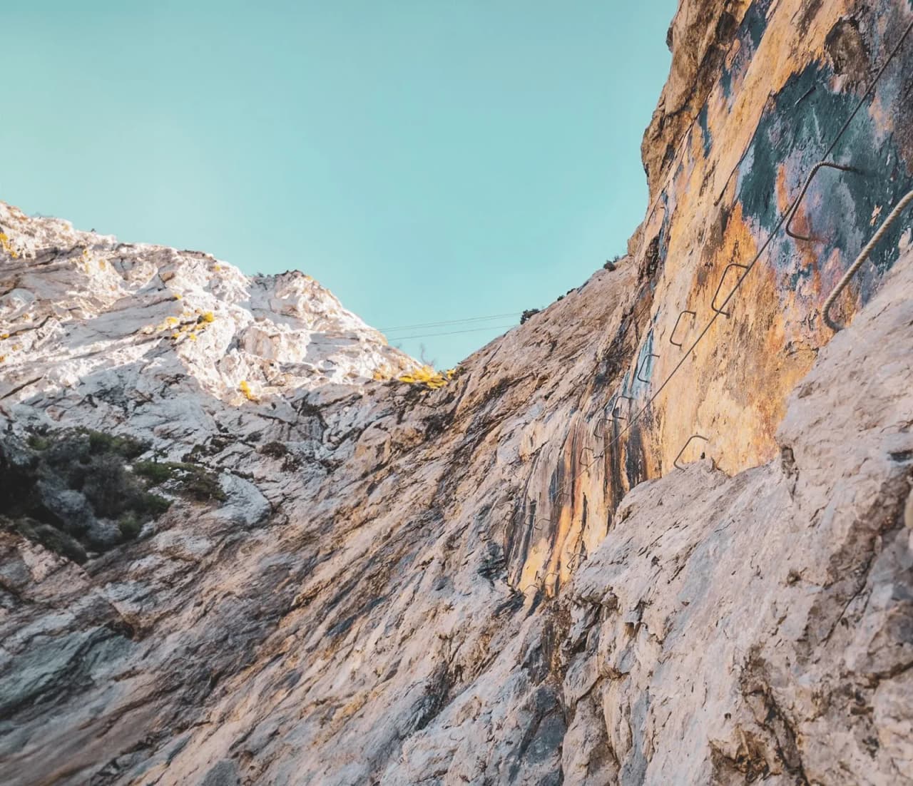 Paroi rocheuse aux couleurs chatoyantes, câbles de via ferrata sous un ciel bleu, invitant à l'aventure.