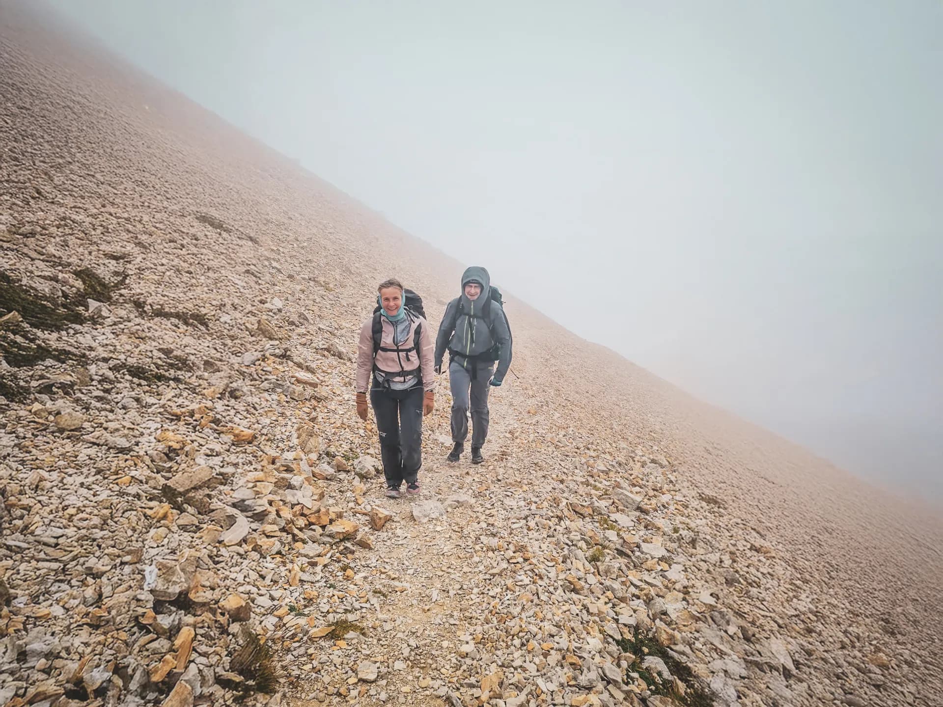 Hikers on an alpine trail, surrounded by enchanting mountain and misty landscapes.