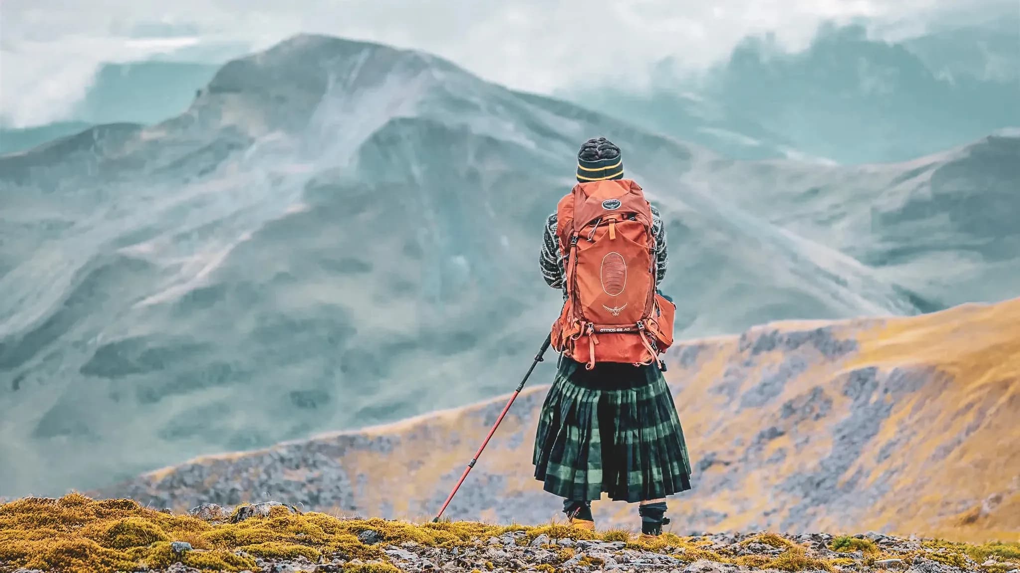 Een wandelaar bewondert de majestueuze landschappen van de Highlands, draagt een kilt en een rugzak.